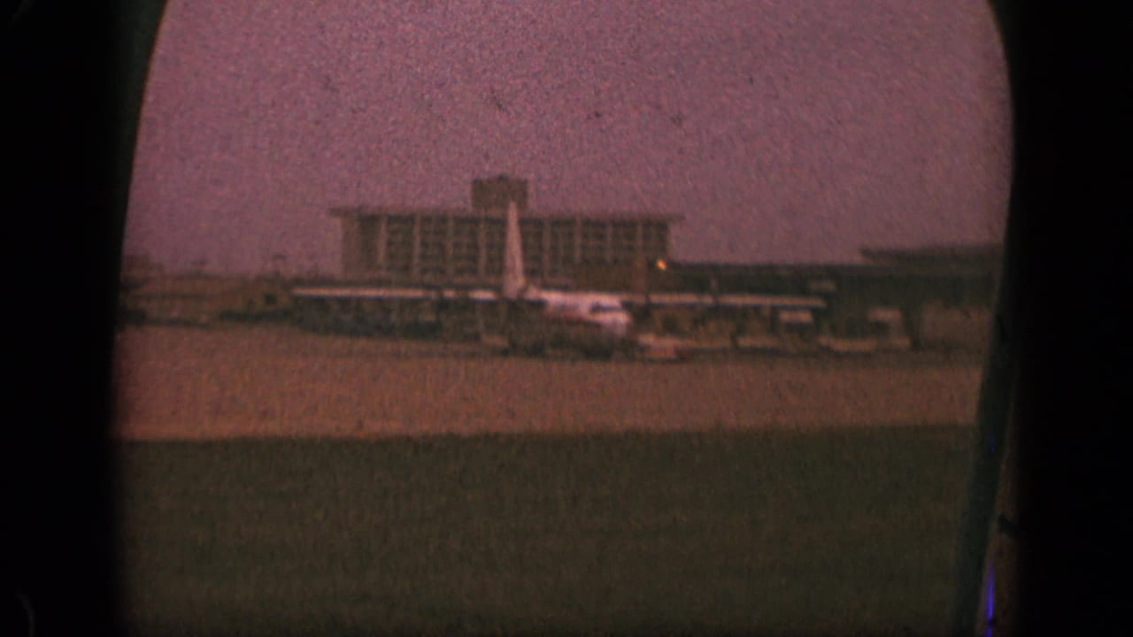 Airport terminal, jet tail, and apron viewed from inside an aircraft.