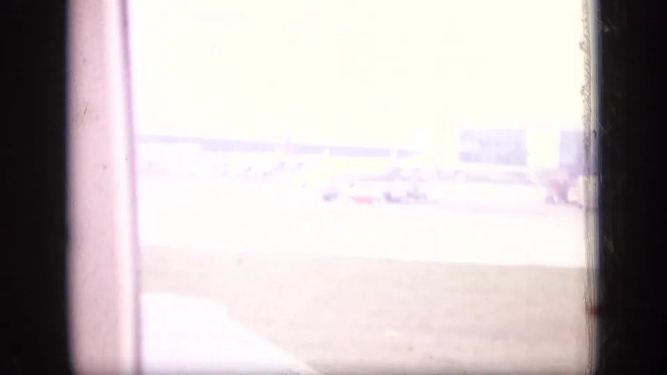 Overexposed final 8mm frame from inside an aircraft, showing a bright airport apron and terminal area in New Jersey.