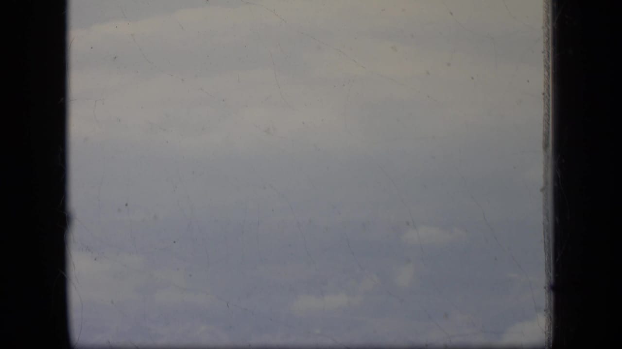 Cloudy sky seen through dark airplane window framing.