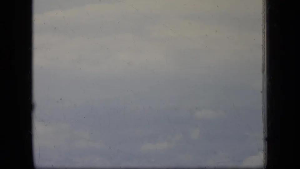 1970 New Jersey home-movie frame looking through an airplane window at a muted cloudy sky.