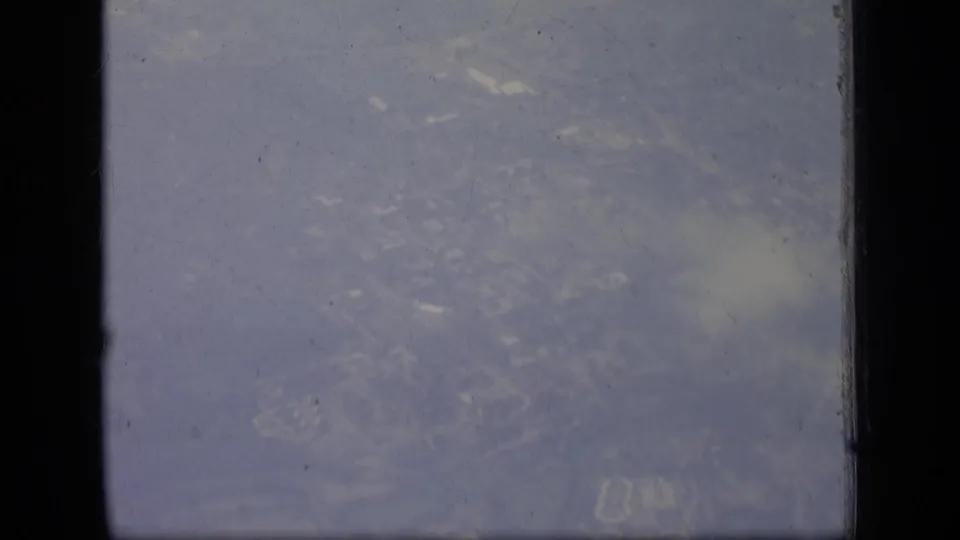 1970 New Jersey aerial home-movie view with faint houses, roads, and trees below the airplane window.