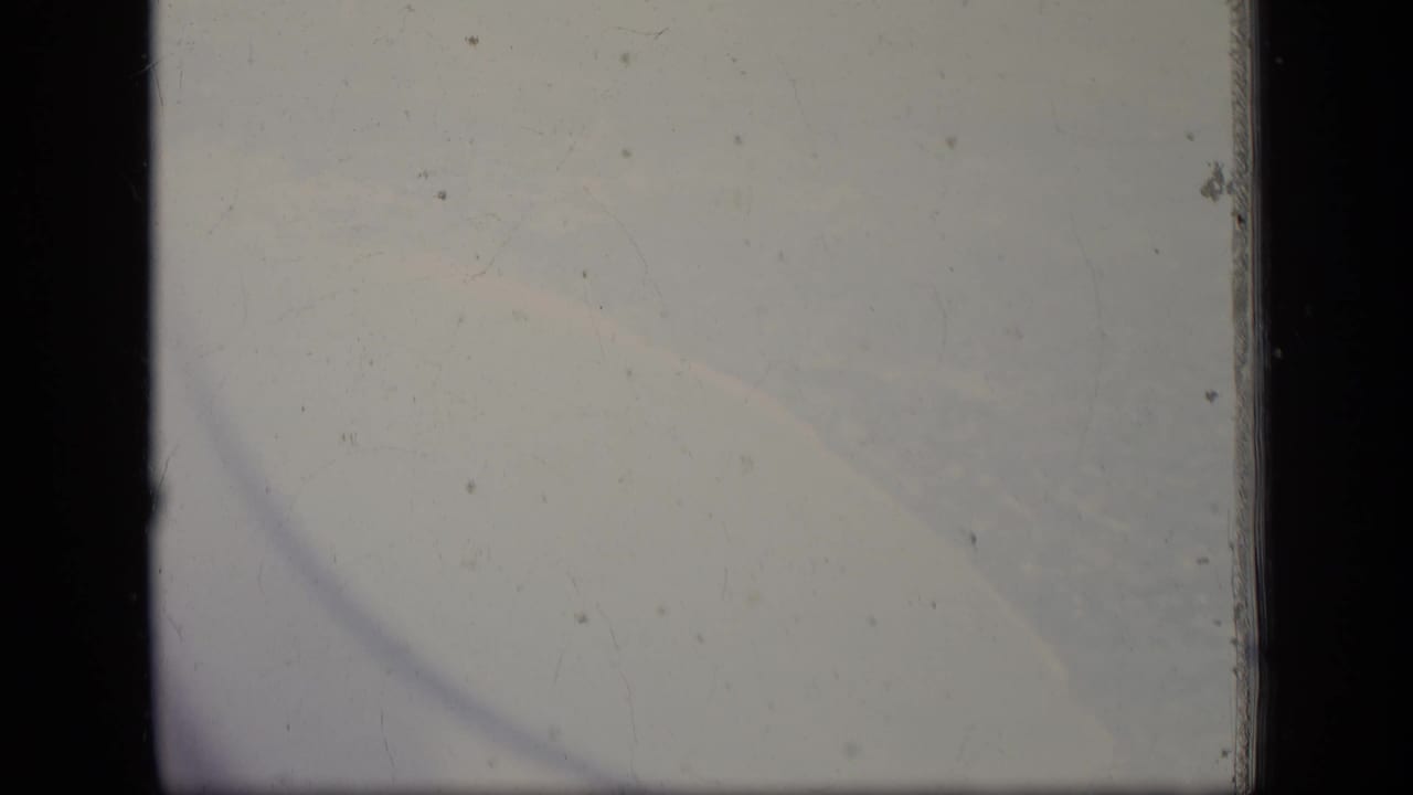 Pale overcast sky seen through dark aircraft-window edges on 8mm film.