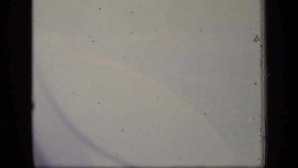 1970 New Jersey 8mm frame showing a hazy sky through an airplane window, with dark borders, dust, and faint scratches.