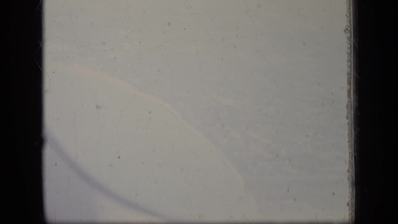 A soft 8mm view from an airplane window over New Jersey, with pale clouds, dark frame edges, and visible film wear.