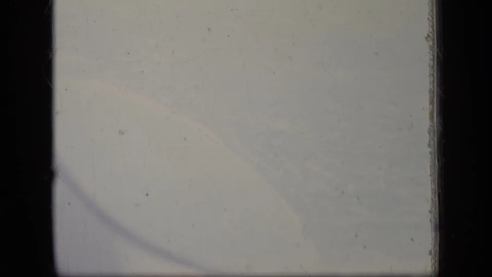 A soft 8mm view from an airplane window over New Jersey, with pale clouds, dark frame edges, and visible film wear.