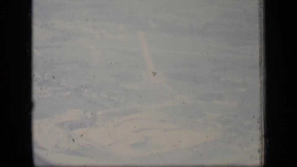 1970 New Jersey 8mm frame with a soft aerial view of a facility area, heavy haze, film scratches, and dark gate borders.