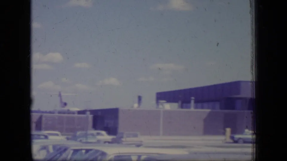 1970 New Jersey ground view of a low modern facility with a purple-toned facade, parked period cars, and bright sky.