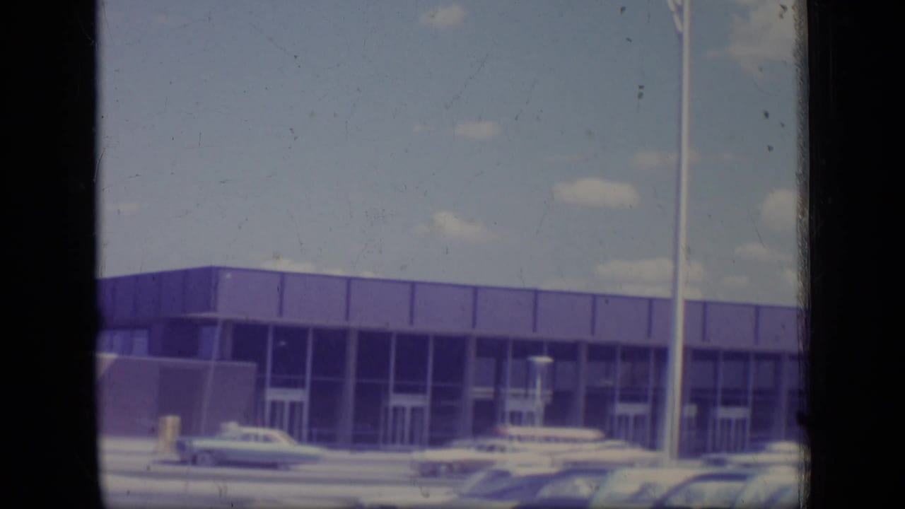 Low modernist building beside a street with several parked or passing cars.