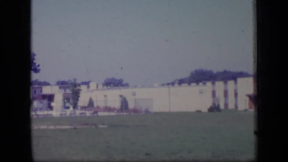 1970 New Jersey 8mm frame showing a beige apartment block, brick accents, lawn, and trees during a slow pan.