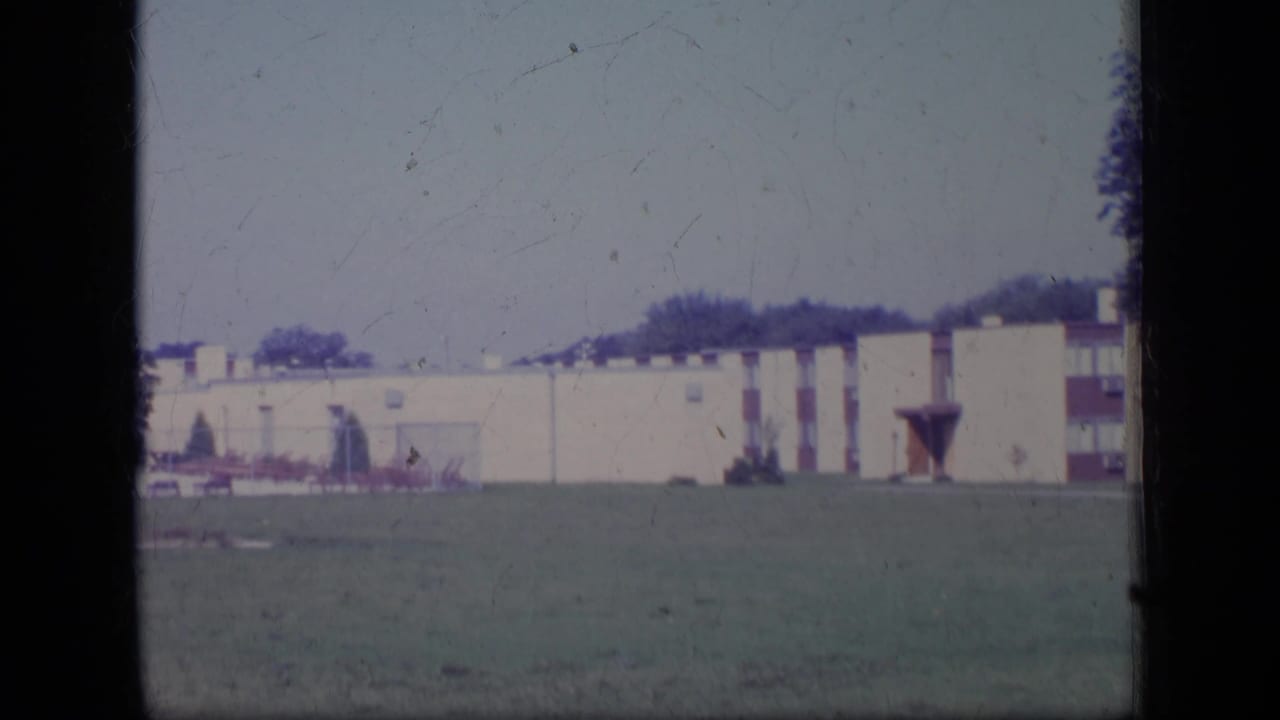 Long cream low-rise building beyond a grassy field, framed by dark film edges.