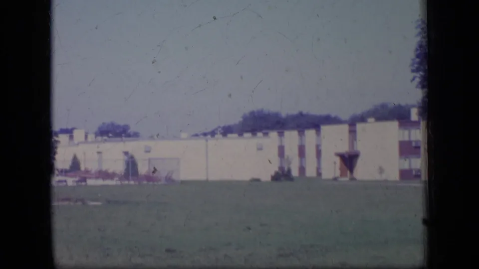 1970 New Jersey 8mm frame showing a cream low-rise building with red accents across an open lawn.