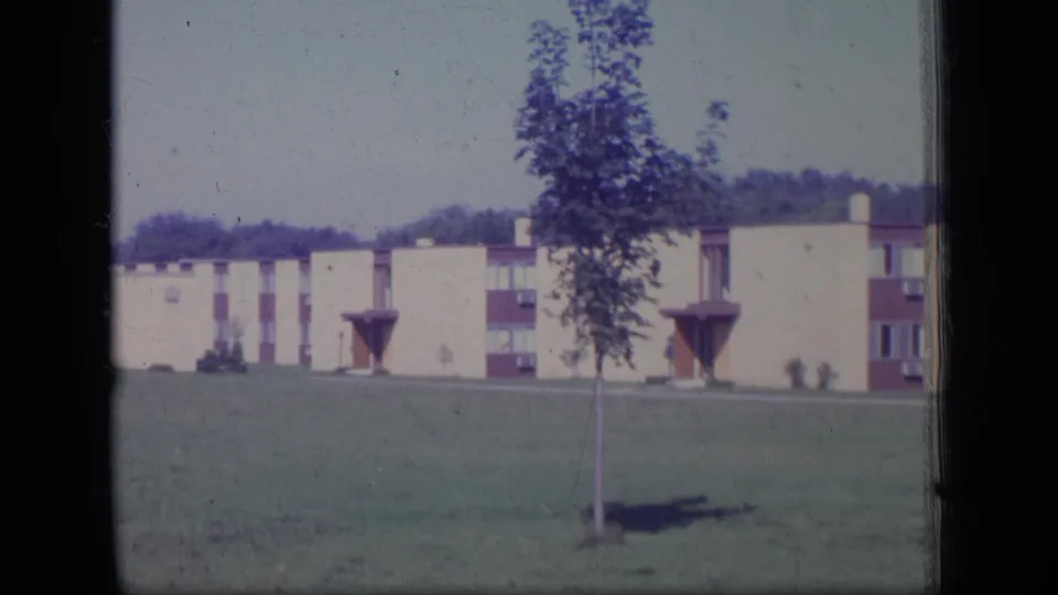 1970 New Jersey 8mm view of low-rise apartment buildings beyond a lawn and young tree, with film borders visible.