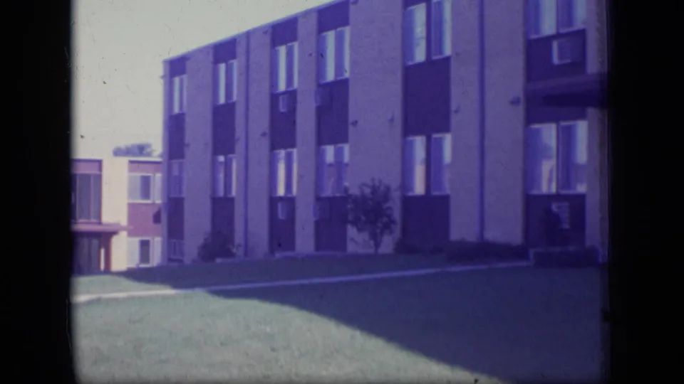 1970 New Jersey 8mm frame of a multi-story apartment building with rectangular windows and lawn in front.