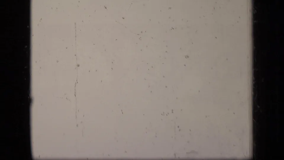 A pale leader-like 8mm frame with dark borders, surface scratches, dust specks, and little visible scene detail.