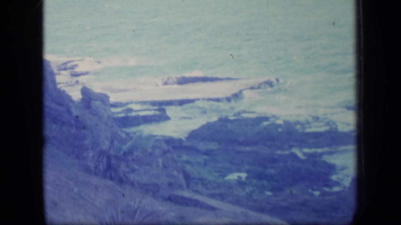 Rocky shoreline and ocean waves seen from a coastal overlook.