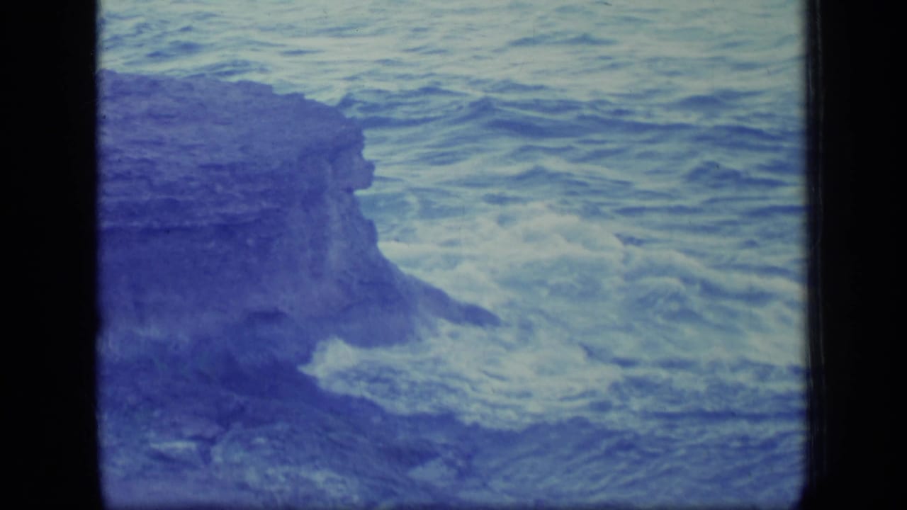 Ocean water churns beside a dark rocky cliff with surf foam near the base.