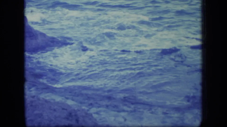 1970 Puerto Rico coastal footage frame with rough water and a partial rocky edge at left.
