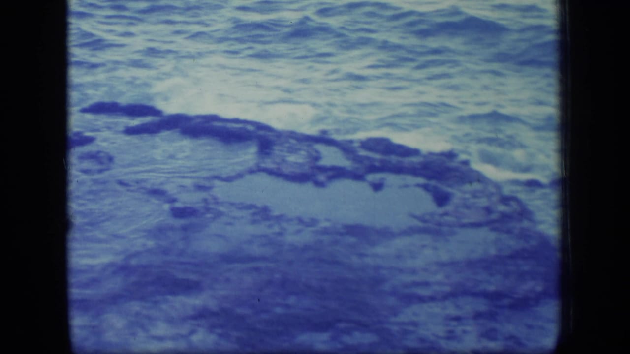 Blue-tinted ocean water beside dark rocks, framed by 8mm film borders.