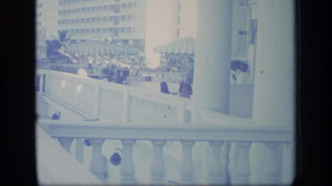 Bright balcony view with white railing, striped umbrellas, plants, and a tall building.