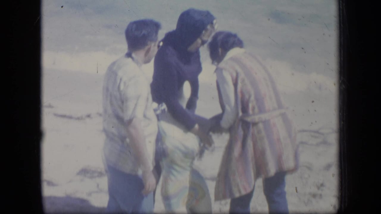 Three people stand outdoors near a bright shoreline or open ground.