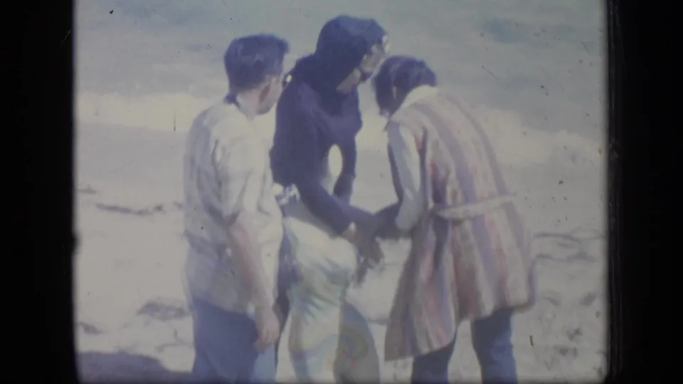1970 Puerto Rico home-movie frame showing three people outdoors in bright light, with one figure bending or leaning near the center.