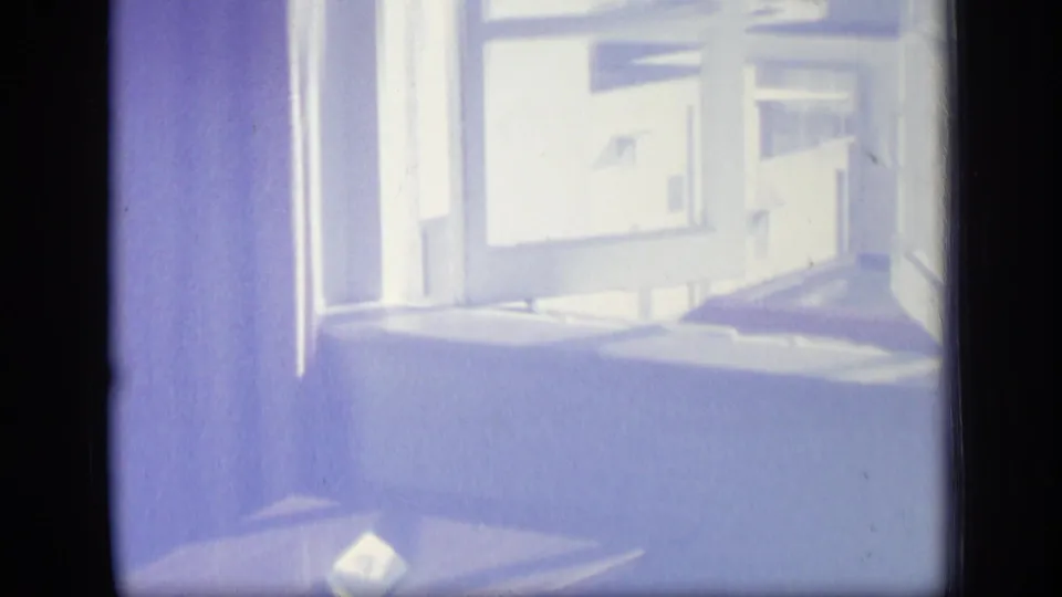 1970 Puerto Rico home-movie frame of a bright interior window, adjacent wall, and small table with a light paper object below.