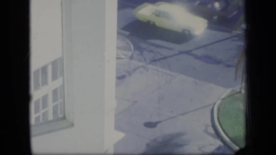 High-angle 1970 Puerto Rico street view with a yellow sedan passing near a white building and curved curb.