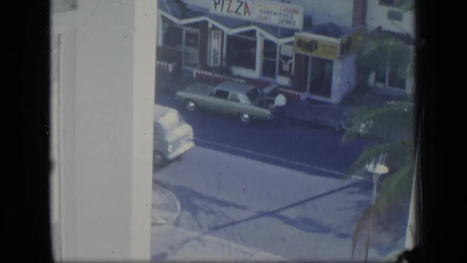 High-angle 1970 Puerto Rico view of a storefront with pizza signage and a green station wagon on the street.