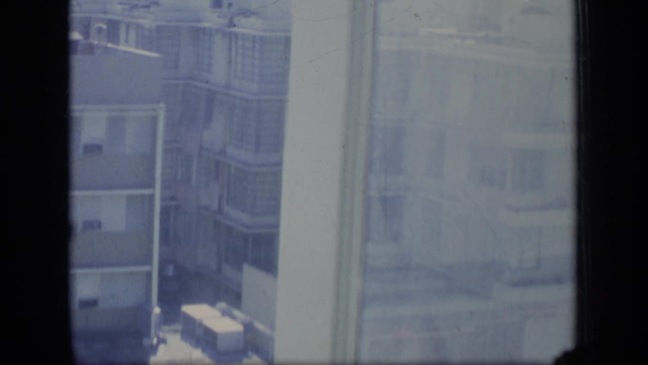 Hazy concrete apartment buildings seen through a window with dark vertical framing.