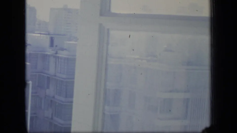 A blue-gray 8mm frame from Puerto Rico in 1970 shows apartment facades and window reflections divided by a dark mullion.
