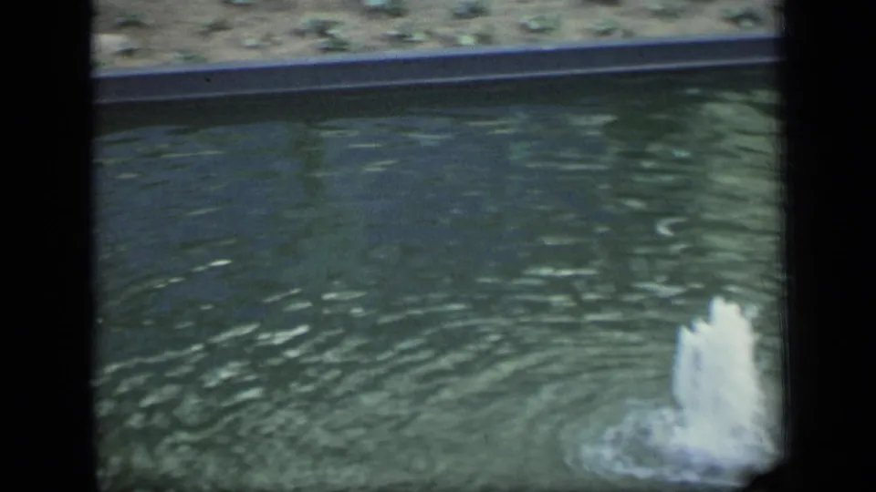 1970 Puerto Rico frame showing a fountain spray at the right, rippling water, a ledge, and dark window framing.