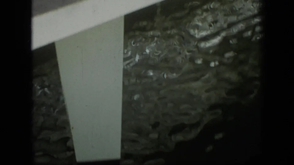 1970 Puerto Rico 8mm frame showing white pedestrian bridge structure above dark green rippling water.