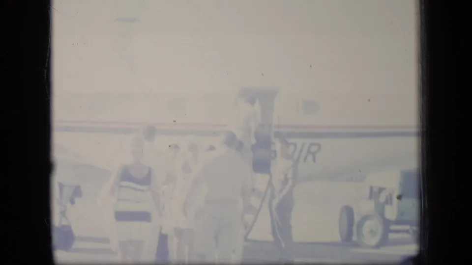 Faded Puerto Rico 1970 home-movie frame showing travelers near an aircraft with partial AIR lettering.