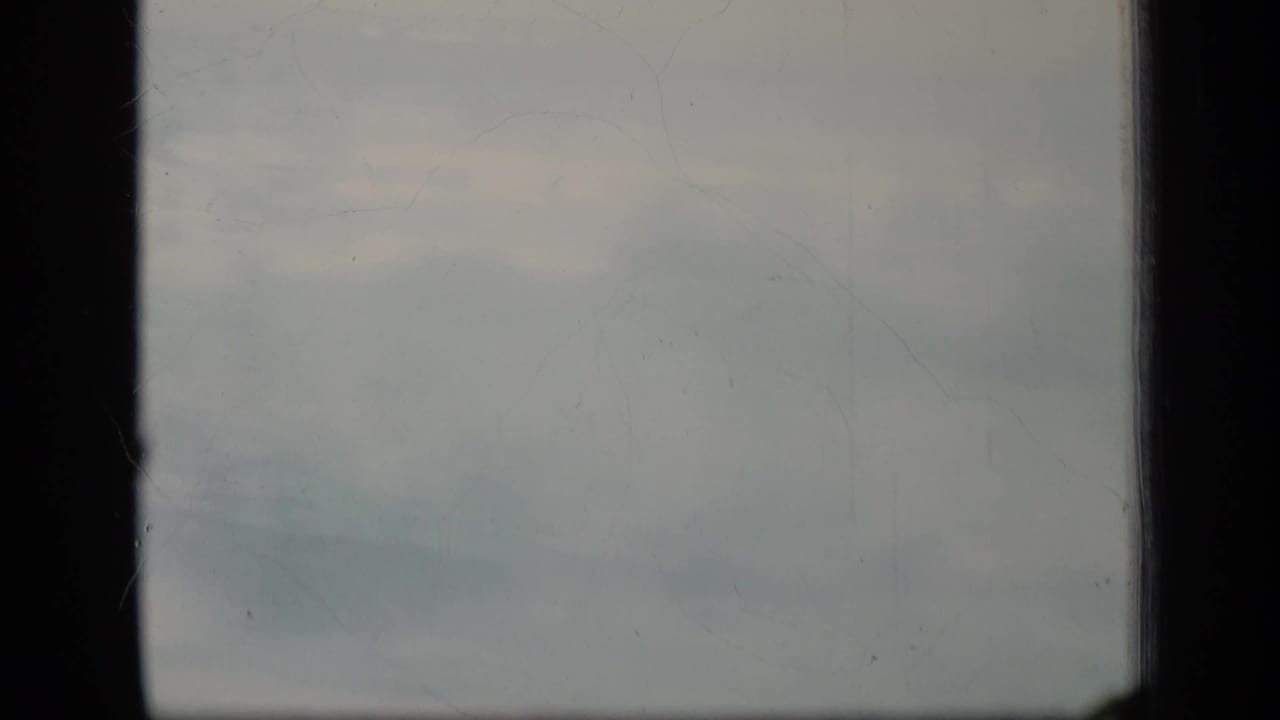 Pale cloudy sky framed by dark film-gate edges.