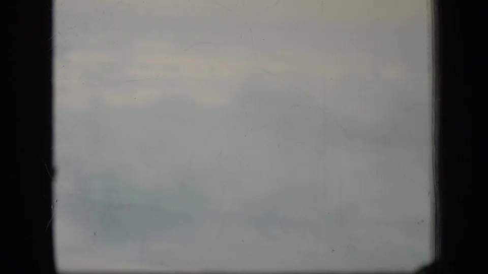 1970 8mm frame likely from Puerto Rico showing pale cloud haze bordered by dark gate edges and surface marks.