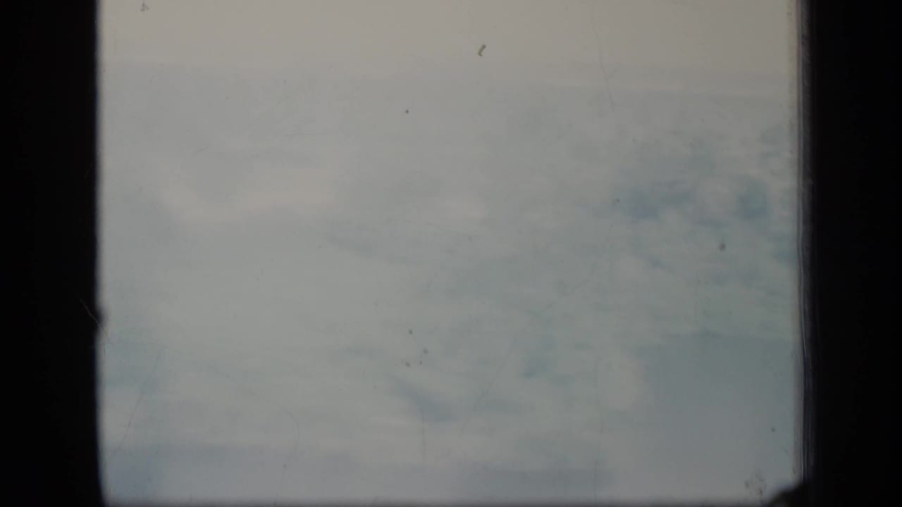 Soft, overcast aerial haze on 8mm film, with dark vertical borders and visible dust marks.