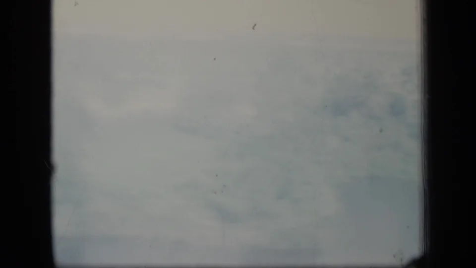 Soft, overcast aerial haze on 8mm film, with dark vertical borders and visible dust marks.