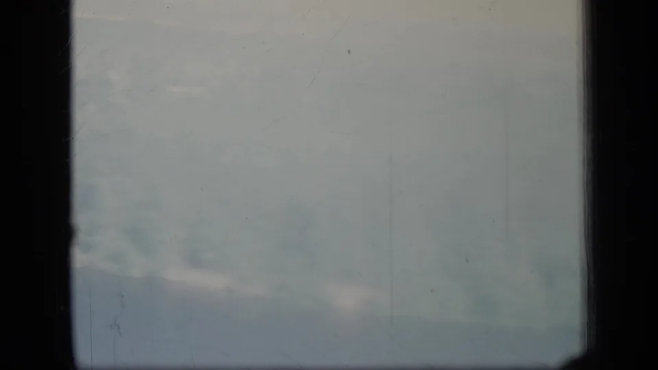 Faint cloud bands and pale haze, likely from a 1970 Puerto Rico travel reel, with visible 8mm scratches and borders.
