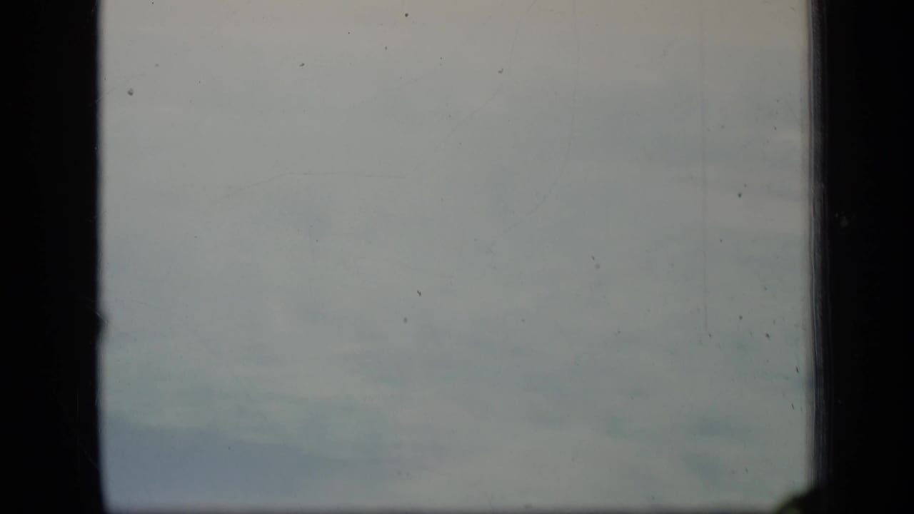 1970 Puerto Rico 8mm frame showing pale clouds through a dark window frame with grain, dust, and soft fading.
