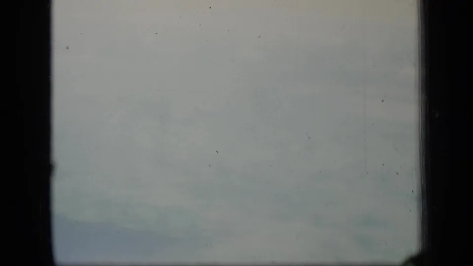 1970 Puerto Rico 8mm frame showing pale clouds through a dark window frame with grain, dust, and soft fading.