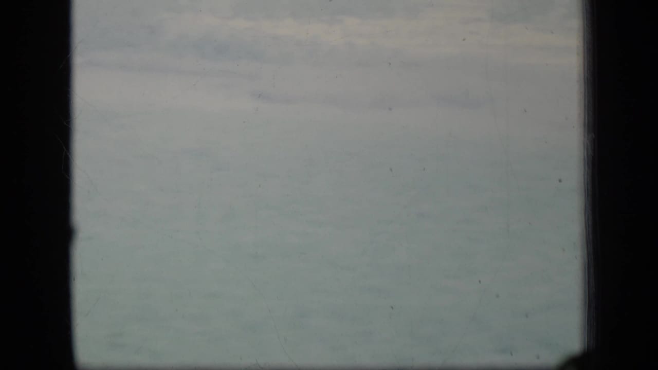1970 Puerto Rico 8mm view of muted cloudy sky divided by a dark window mullion, with light film wear visible.