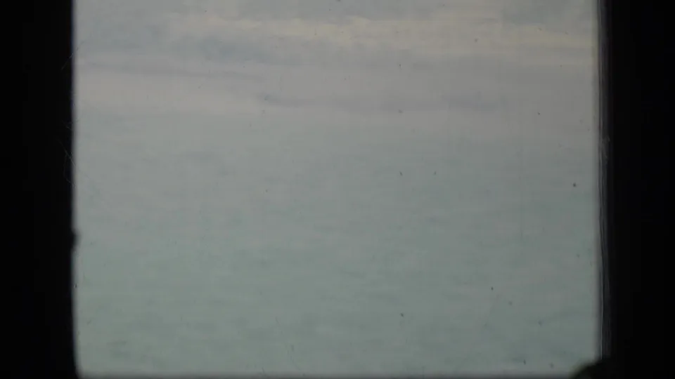 1970 Puerto Rico 8mm view of muted cloudy sky divided by a dark window mullion, with light film wear visible.