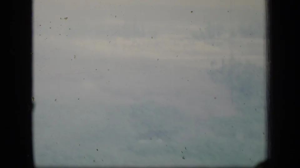 1970 Puerto Rico 8mm frame with a dark window crossbar over a cloudy sky, showing grain, dust, and color fading.
