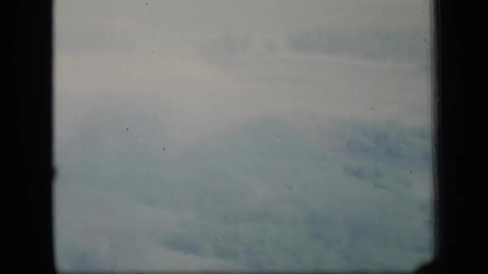 1970 Puerto Rico 8mm frame of blue-gray clouds seen through a dark window grid, with visible grain and dust.
