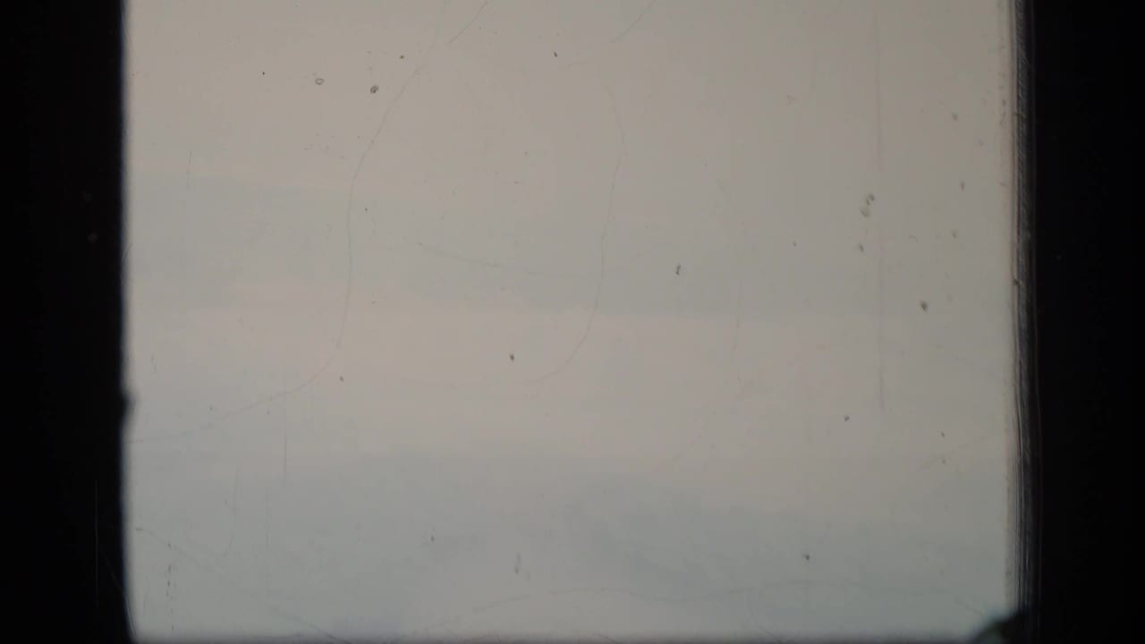 1970 Puerto Rico 8mm frame showing a soft, hazy aerial view with pale sky, faint terrain, dust, and dark film borders.