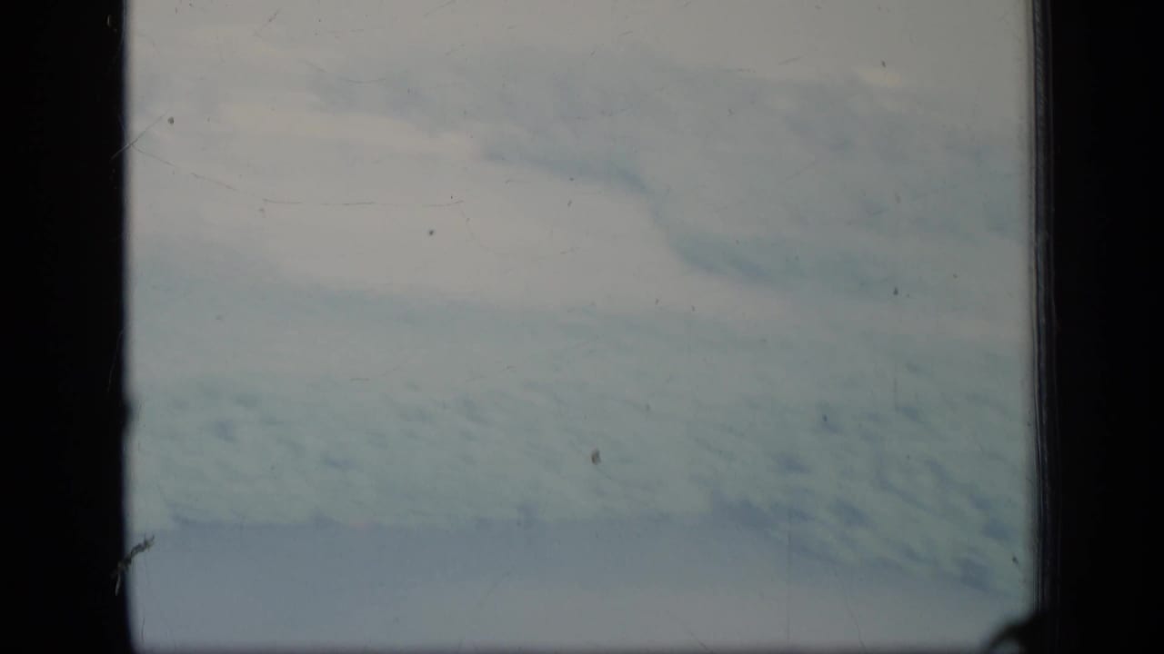 1970 Puerto Rico 8mm frame with cloudy sky and blurred blue-green ground or water seen from a low-flying plane.