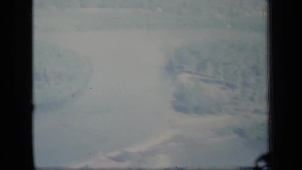 1970 Puerto Rico 8mm aerial frame showing pale haze, soft landscape shapes, and dark gate edges during low flight.