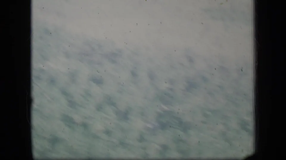 1970 Puerto Rico 8mm frame with a muted blue-green aerial landscape, cloud cover, dust specks, and dark frame edges.