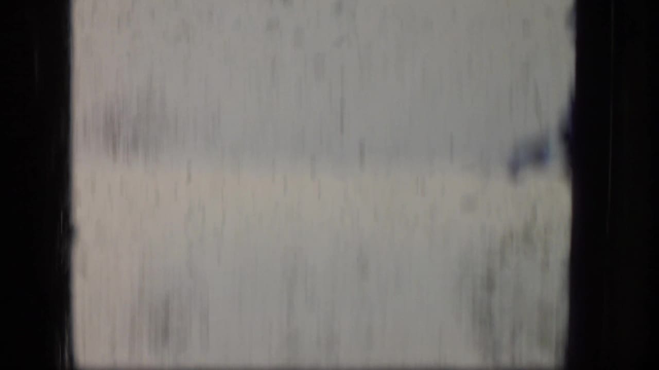 1970 Puerto Rico 8mm frame showing a soft, blurred airplane-window view with dark window bars and hazy terrain outside.