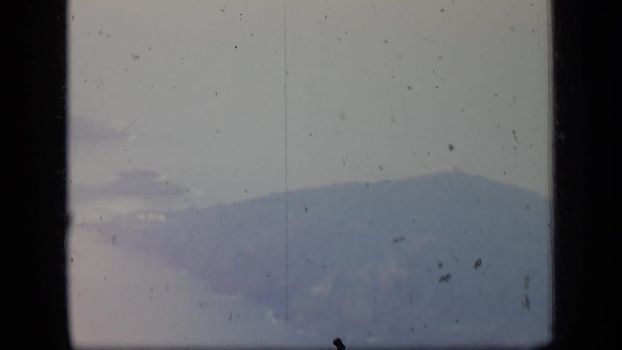 1970 Puerto Rico aerial frame with a distant hazy mountain silhouette visible through the airplane window and aged film texture.